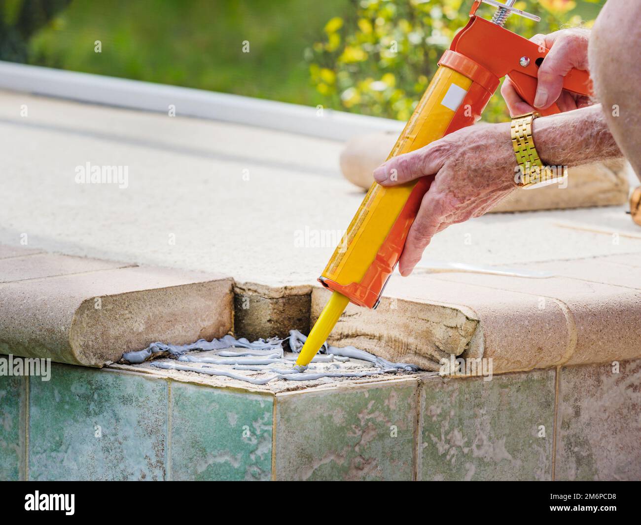 Homme appliquant de la colle de ciment avec un outil pistolet à calfeutrer. Réparation de carreaux de piscine en pierre de finisseur en béton cassé. Banque D'Images