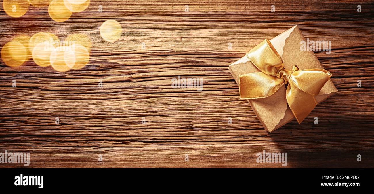 Boîte cadeau en papier Kraft avec noeud en ruban doré sur une texture en bois ancienne Banque D'Images