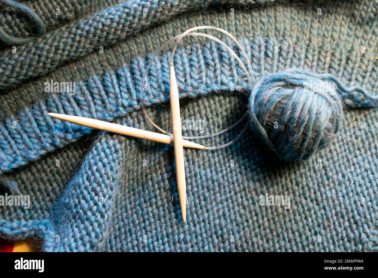 Aiguille à tricoter circulaire sur fond de bleu grosse laine boule de laine tricotée main pull chandail Wales UK KATHY DEWITT Banque D'Images