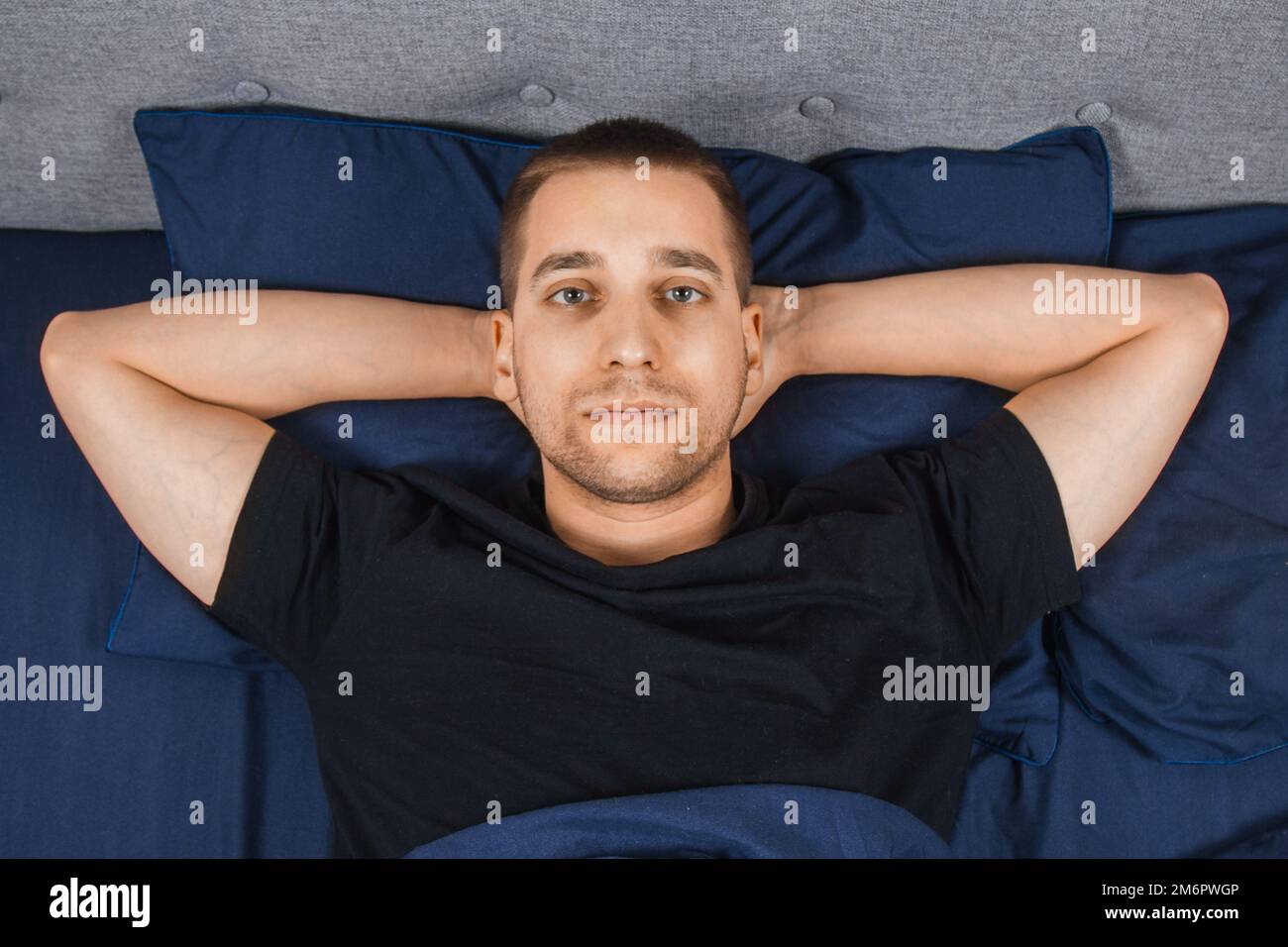 Vue de dessus d'un beau jeune homme souffrant d'insomnie ayant de la difficulté à s'endormir sur son lit dans sa chambre la nuit. Chambre Bachelor. Problèmes de sommeil. Banque D'Images