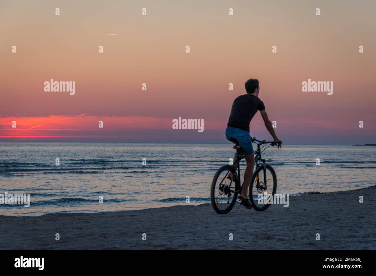 Arrière d'un homme qui fait du vélo sur la plage de Liepaja au coucher du soleil Banque D'Images