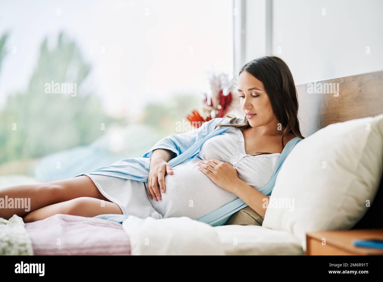 Portrait de la femme enceinte heureuse se détendre allongé dans le lit et touchant son ventre à la maison. Banque D'Images