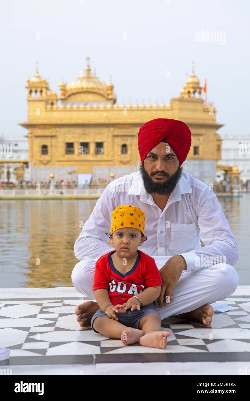 Sikh indien en costume blanc et pieds nus avec son fils assis au bord du bassin d'eau de l'Amrit Sagar ou du lac Sacré, au Hari Mandir Or Banque D'Images