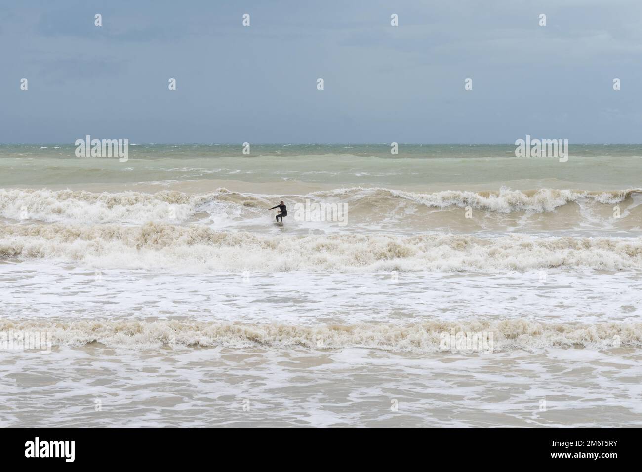 Surfer sur une vague saccadée dans les mers orageux de la Manche dans l'est du Sussex Banque D'Images