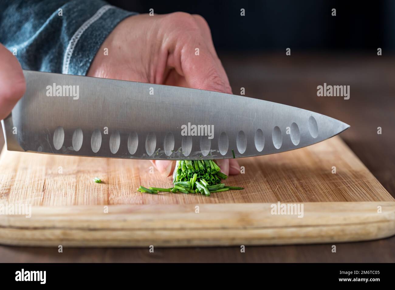 Gros plan sur les mains d'un chef coupant un paquet de ciboulette sur une planche en bois. Banque D'Images