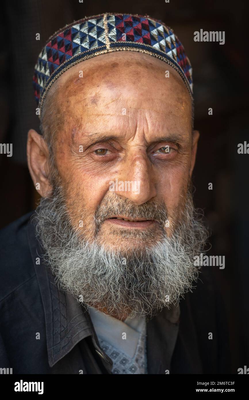 Kulob, Khatlon, Tadjikistan - 08 21 2019 : Portrait en gros plan du vieil homme tadjik avec une barbe portant une calotte crânienne traditionnelle sur fond sombre Banque D'Images