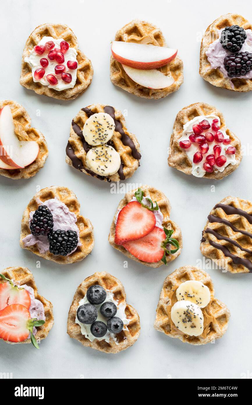 Mini-gaufres en forme de cœur avec différentes garnitures disposées en rangées. Banque D'Images