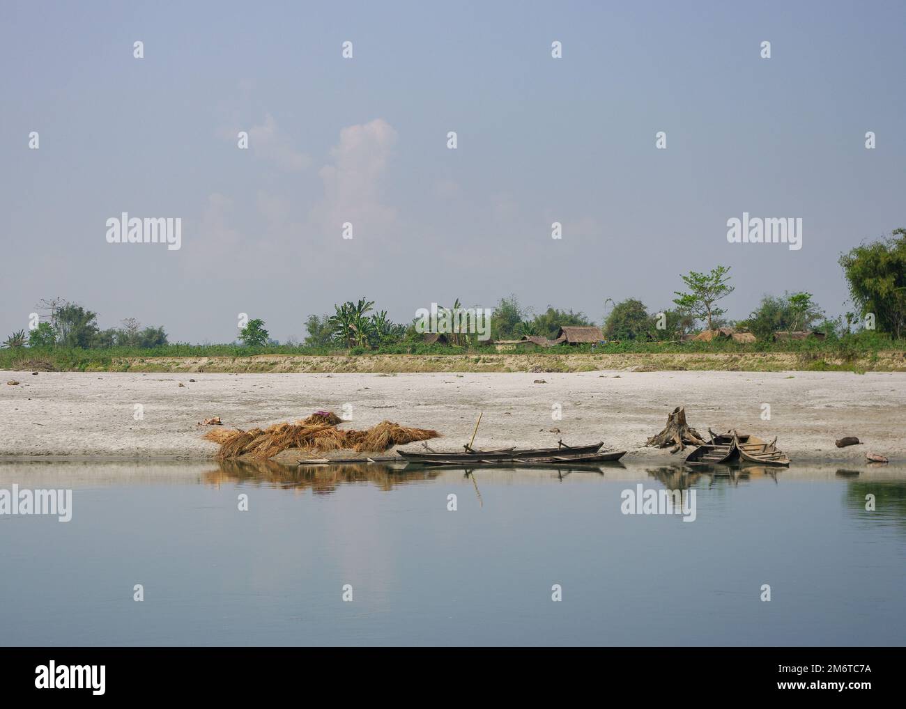 Paysage rural vue sur la rive de la rivière Brahmaputra avec des bateaux de pêche en bois et village en arrière-plan, Assam, Inde Banque D'Images