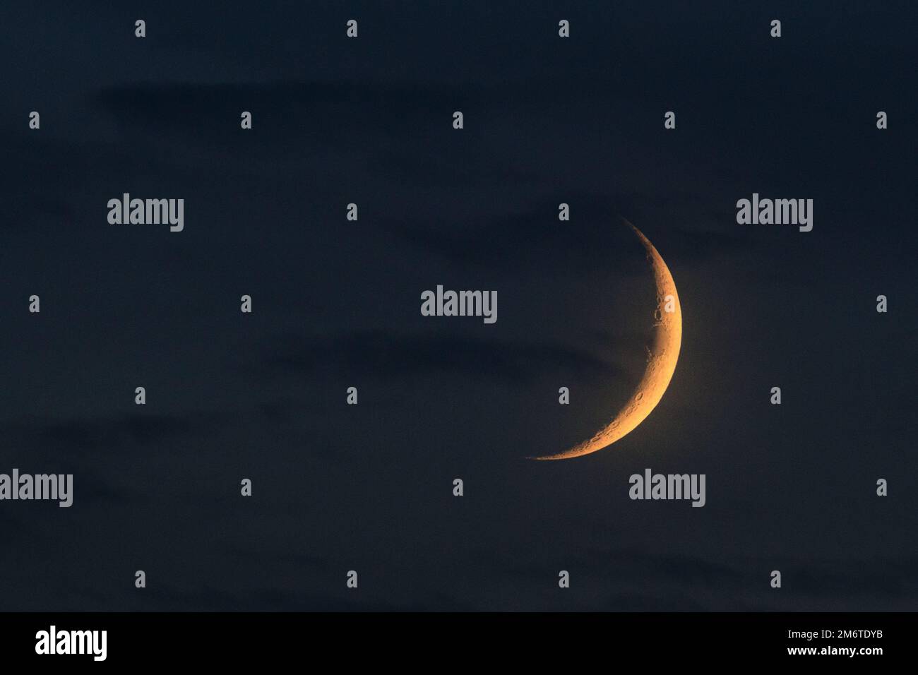 Jeune croissant de lune isolé mis en évidence par le soleil le soir. Sur fond bleu ciel nuageux. Photographie astronomique Banque D'Images