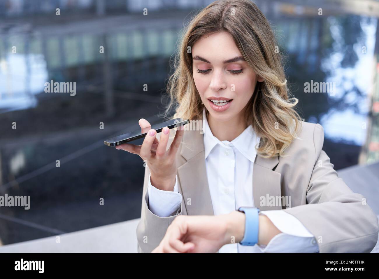 Femme d'affaires vérifie l'heure sur la montre numérique et enregistre les messages vocaux, organise une réunion, se trouve à l'extérieur du centre-ville Banque D'Images