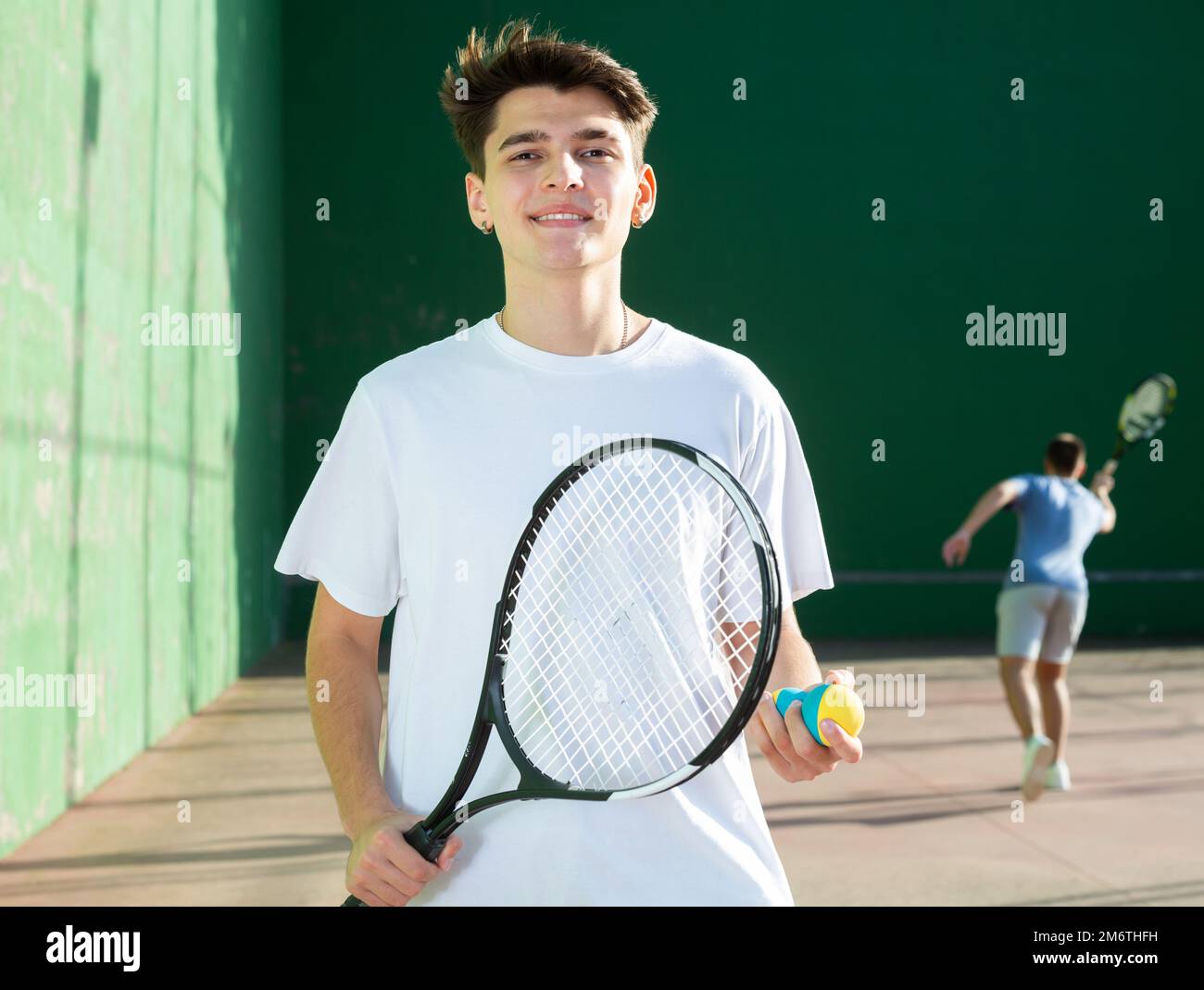 Portrait d'un garçon caucasien debout sur la cour frontenis, tenant la raquette et le ballon Banque D'Images