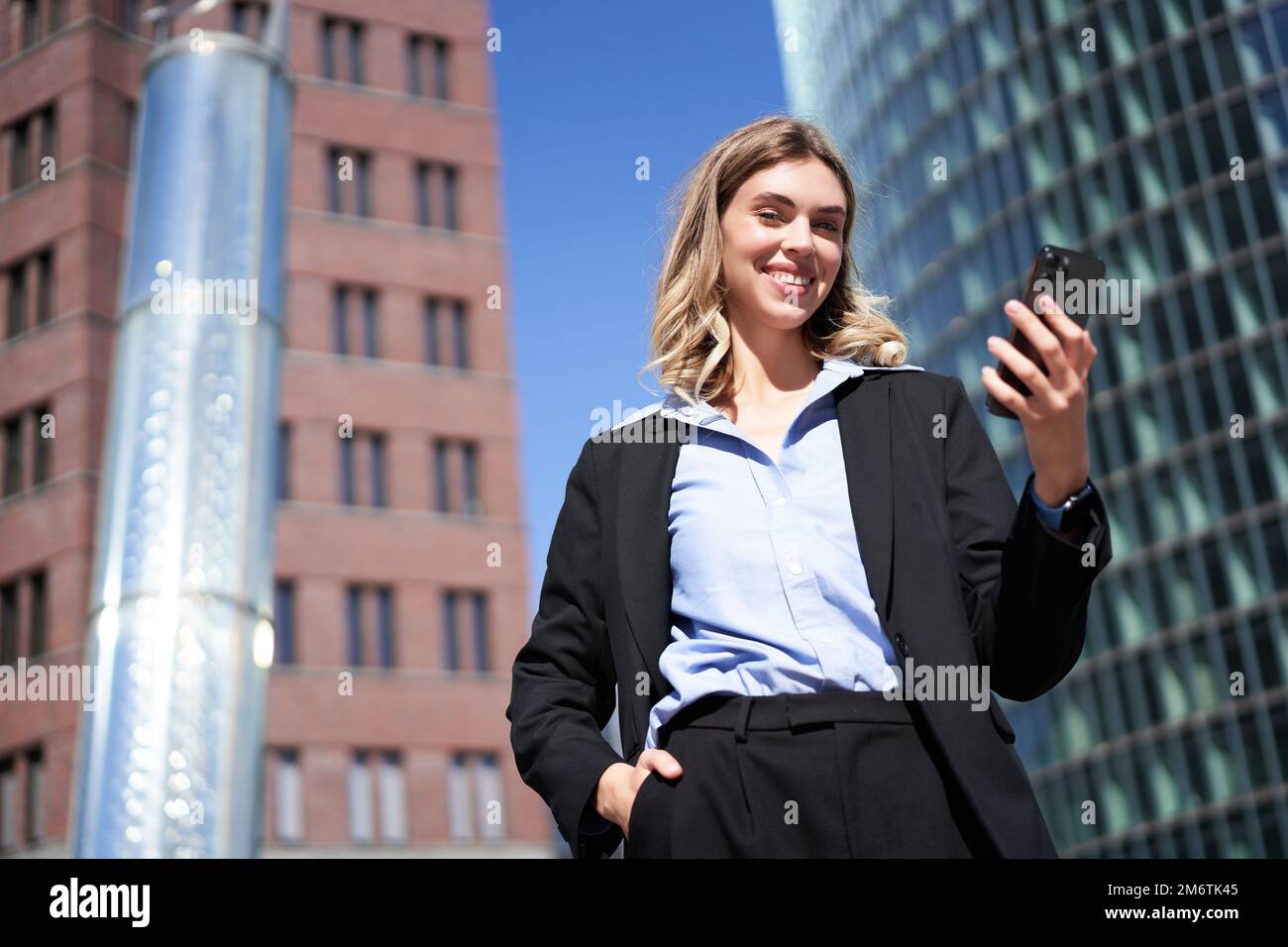 Prise de vue en contre-plongée d'une femme d'affaires en costume, debout dans la rue et regardant un téléphone portable, tenant un smartphone Banque D'Images