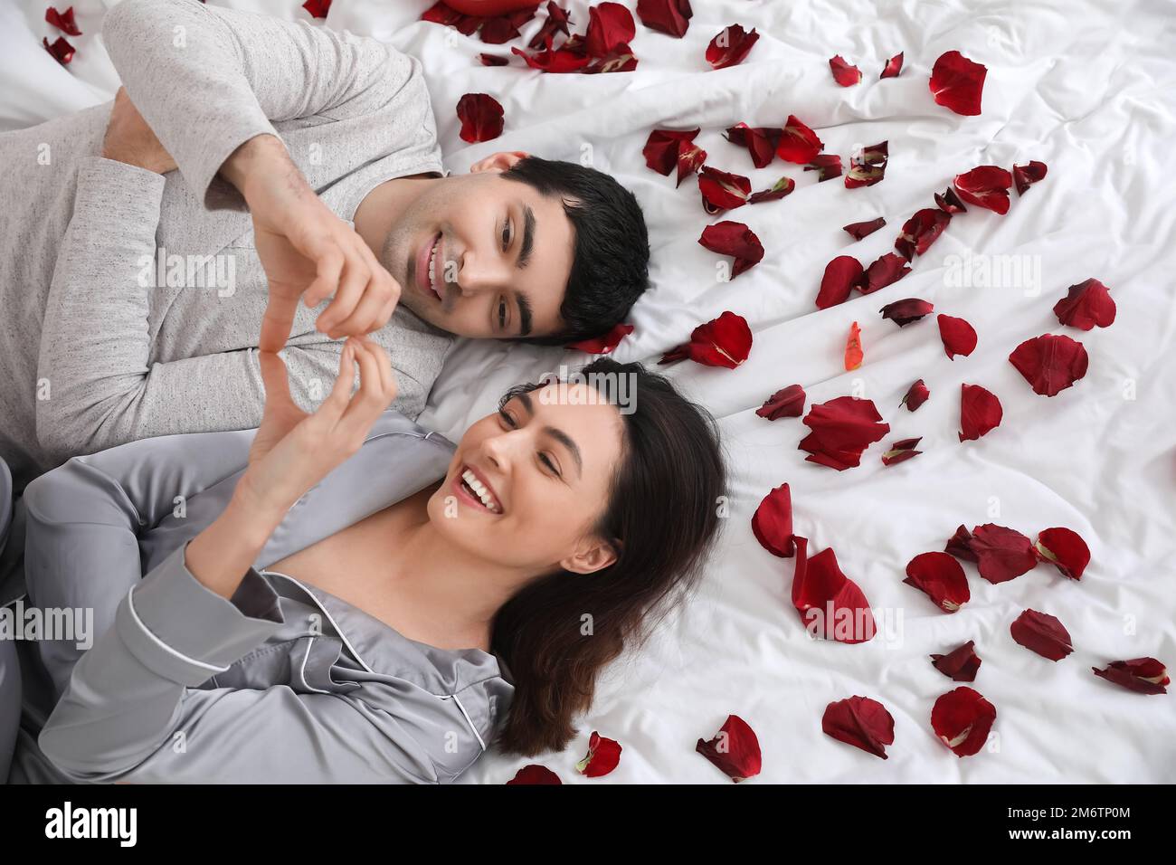 Jeune couple en forme de coeur avec leurs mains au lit le jour de la Saint-Valentin, vue du dessus Banque D'Images