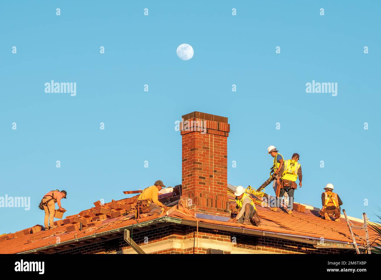 New Orleans, LA, USA - 4 JANVIER 2023: Ouvriers remplaçant les tuiles de toiture sur un toit avec la lune en arrière-plan Banque D'Images