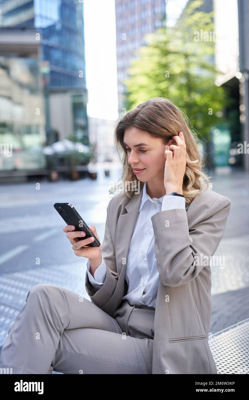 Portrait vertical de la femme en costume à l'aide d'un téléphone portable, de la lecture de messages ou de l'application de vérification, en posant à l'extérieur Banque D'Images