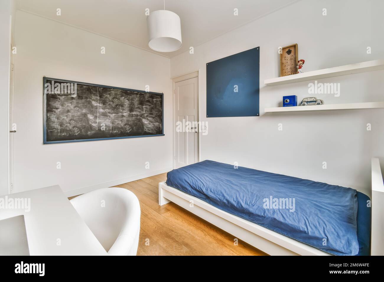 une pièce blanche avec des draps bleus sur le lit, et un tableau noir dans le mur derrière il est un tableau de craie qui dit Banque D'Images