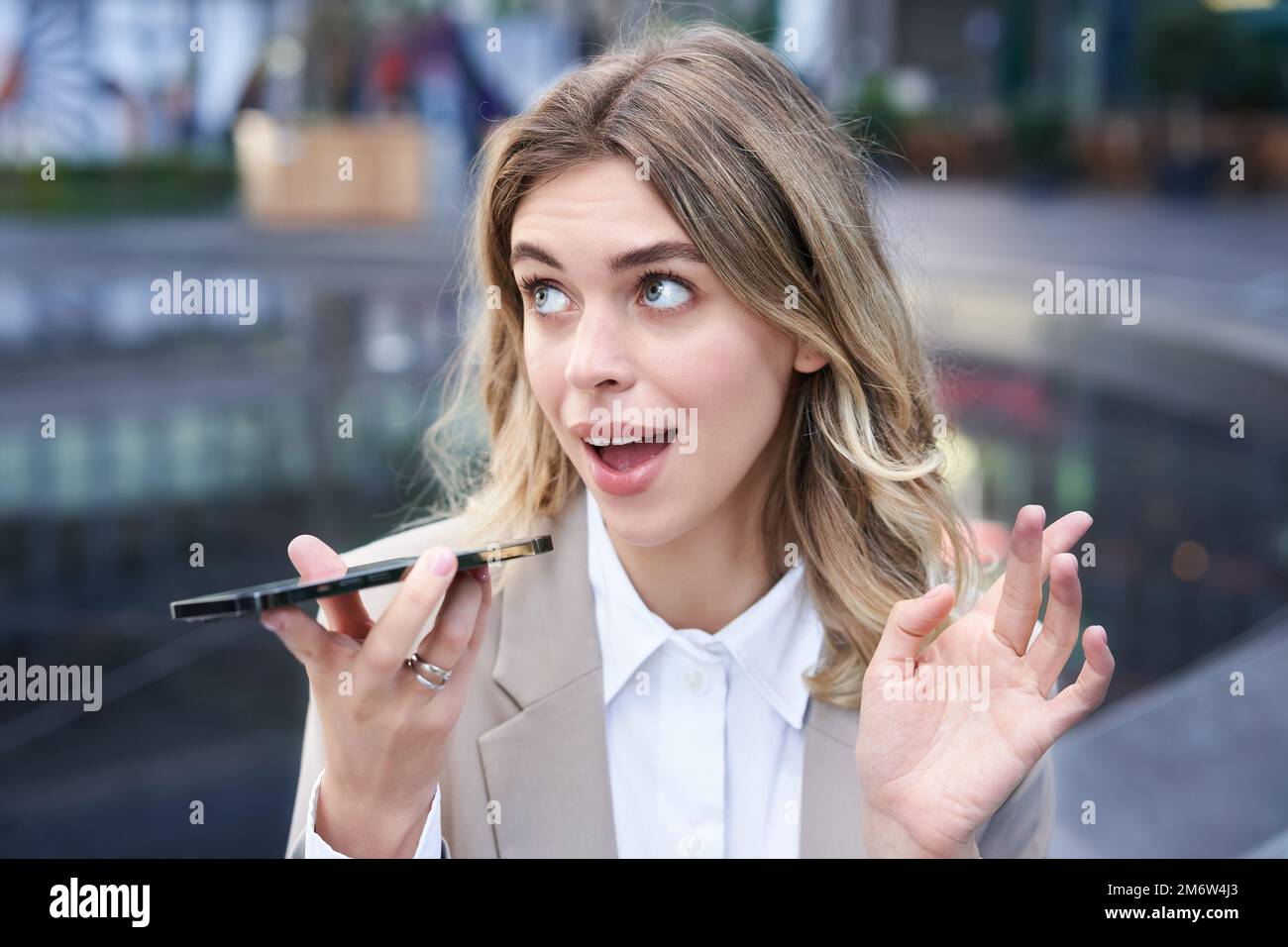 Femme d'affaires bavardeuse assise au centre-ville et enregistrant un message vocal, parlant dans le microphone du smartphone Banque D'Images