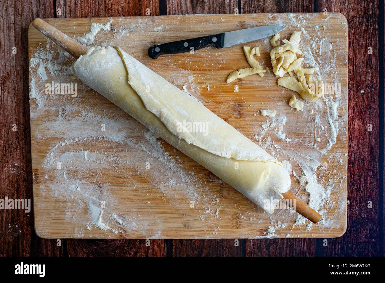 Pâte à tarte enroulée autour d'un rouleau en bois : pâte à pâtisserie enroulée et taillée avec des outils de cuisson Banque D'Images