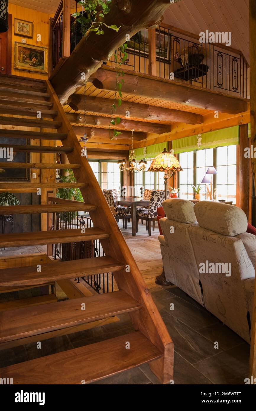 Escaliers en rondins teints menant à l'étage supérieur et à l'arrière du canapé gris dans le salon à l'intérieur de la maison en rondins. Banque D'Images
