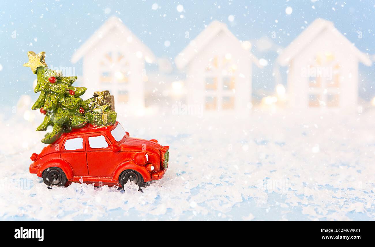 Décoration de Noël - voiture rétro rouge sur la neige passe devant des maisons blanches avec des guirlandes de lumières dans le bokeh CHRI Banque D'Images