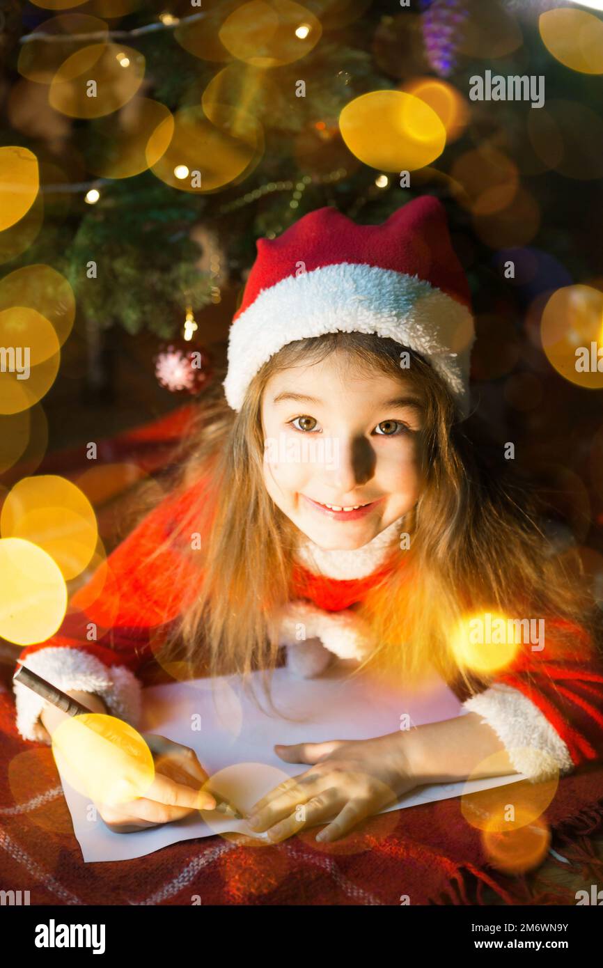 Petite fille dans un chapeau de père Noël et robe rouge sous l'arbre de