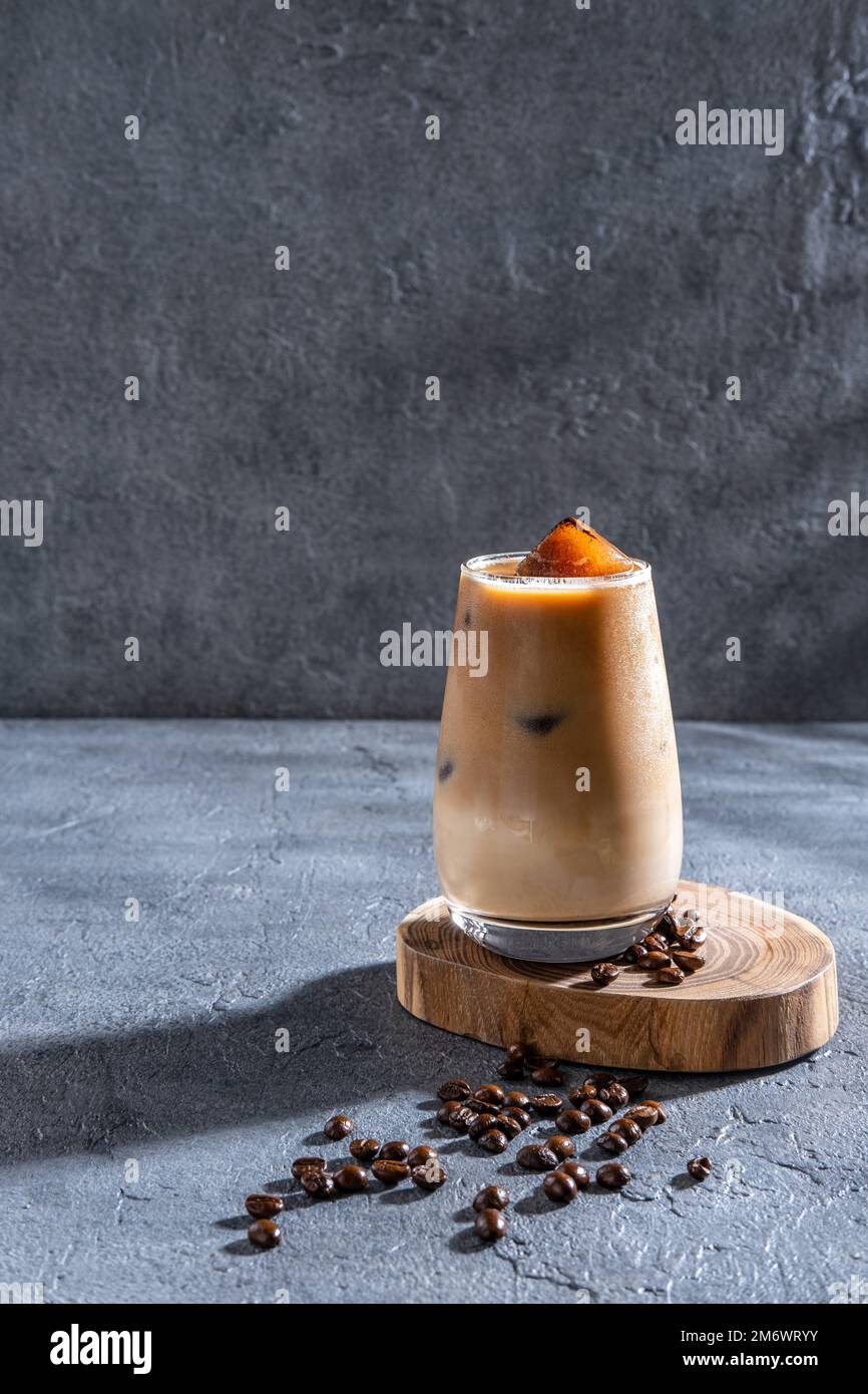 Du café glacé dans un grand verre avec de la crème versée et des grains de café. Boisson froide au café sur fond sombre avec espace de copie. Banque D'Images