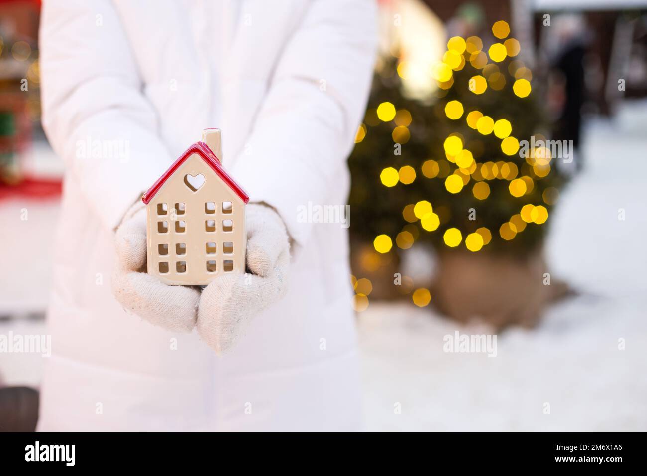 Maison, petite maison dans les mains de femme portant des mitaines et des vêtements chauds dehors dans la neige. Affaire pour l'immobilier, achat, con Banque D'Images