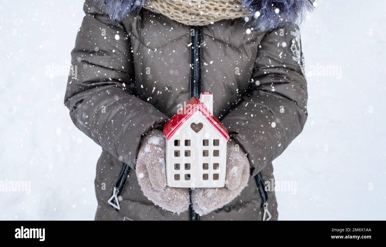 Maison, petite maison dans les mains de fille portant des mitaines et des vêtements chauds dehors dans la neige. Valeurs familiales, achat de logements, rel Banque D'Images