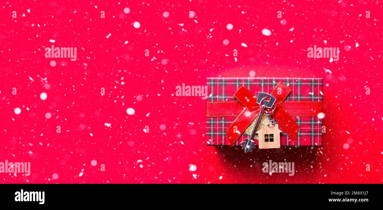 Clé maison avec porte-clés cottage. Joyeux nouvel an sur fond rouge avec neige, cadeau, carte de vœux. Achat, construction, relocatio Banque D'Images