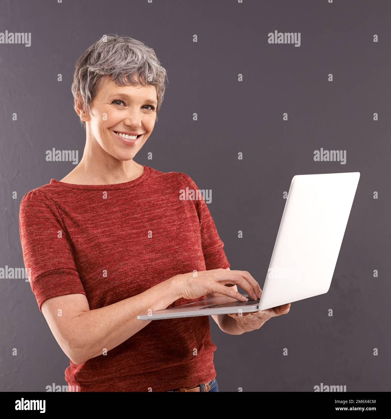Mature et moderne. Portrait studio d'une femme âgée tenant un ordinateur portable sur fond gris. Banque D'Images