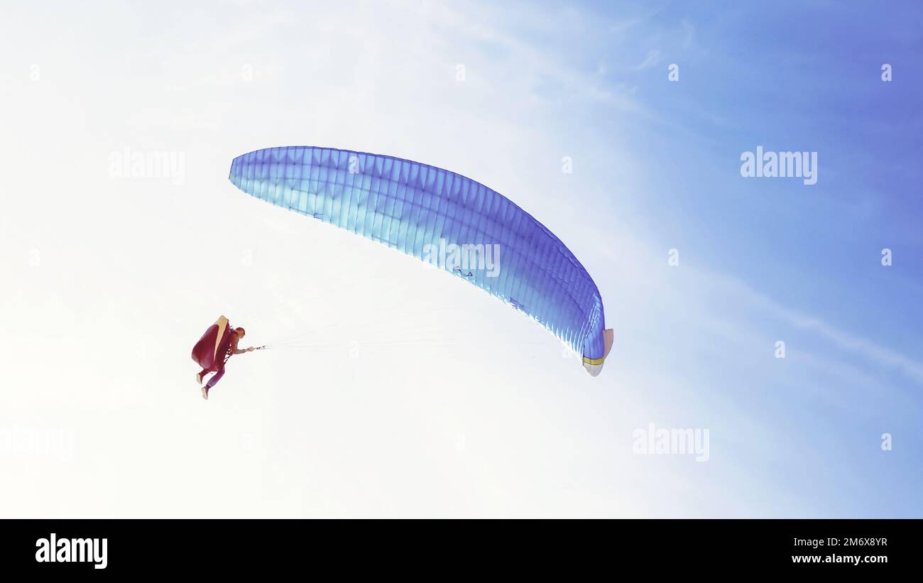 Parapente avec aile bleue volant dans le ciel bleu Banque D'Images