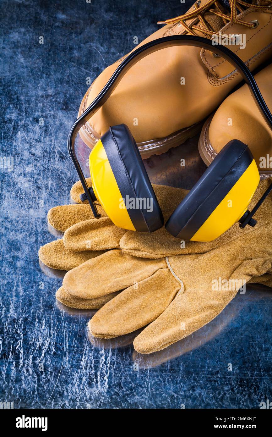 Chaussures de travail en cuir gants de protection et écouteurs de réduction du bruit sur surface métallique rayée concept de construction. Banque D'Images