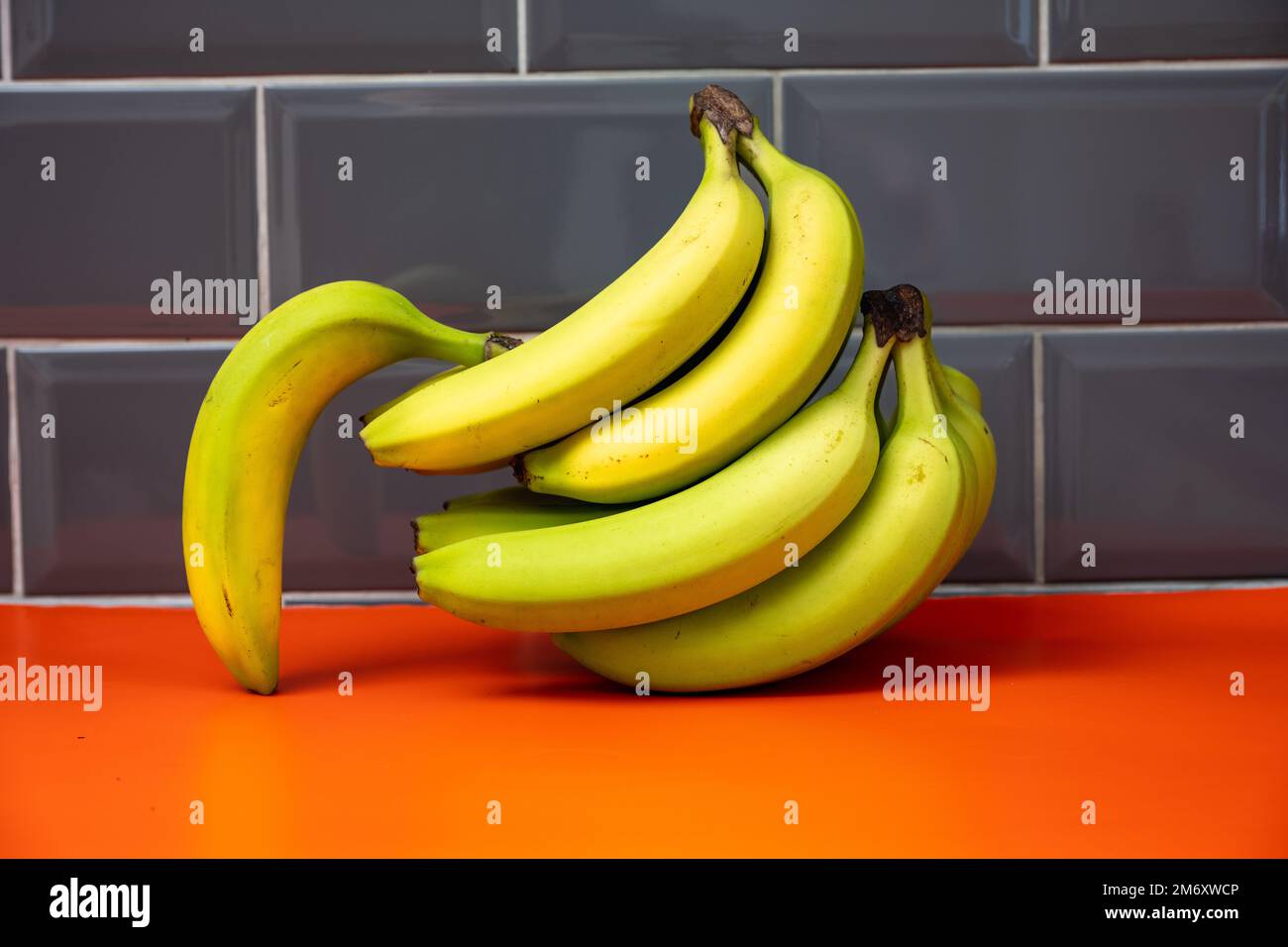 bananes non mûres en vrac sur fond orange sur fond gris Banque D'Images