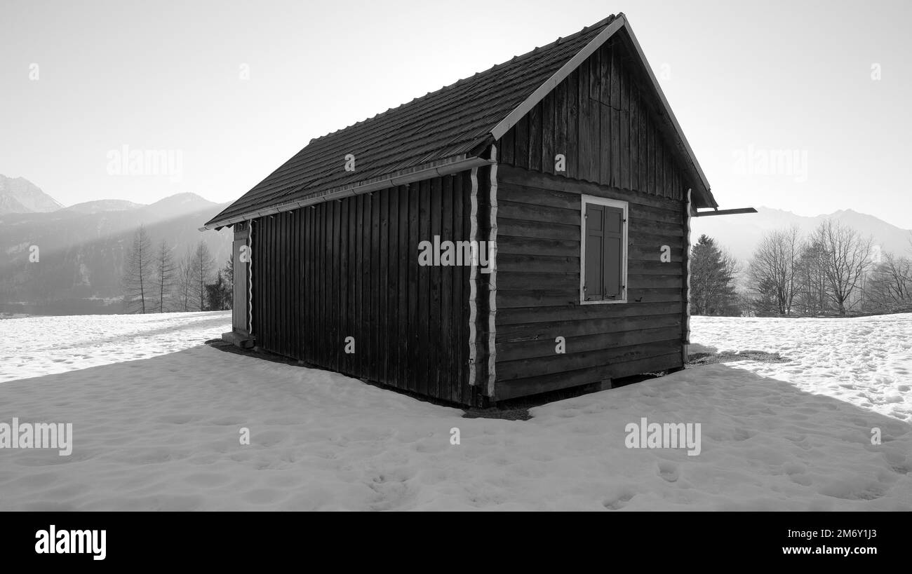 Cabane en bois avec toit en pignon dans la neige avec brouillard et forêt en arrière-plan en noir et blanc en Autriche Banque D'Images