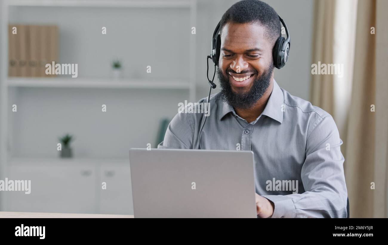 Souriant heureux Africain américain ethnique homme d'affaires soutien aide agent ligne Manager travailleur en ligne professeur dans casque homme dans le bureau parler Banque D'Images