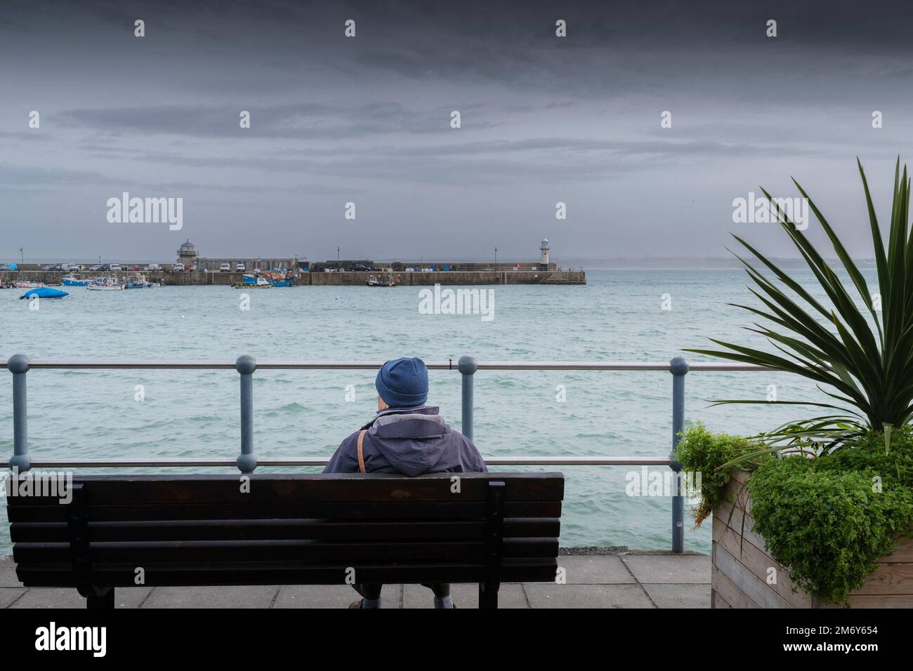 Météo au Royaume-Uni. Un homme assis sur un banc donnant sur Smeatons Pier lors d'une journée pluvieuse et misérable dans la ville balnéaire historique de St Ives, dans les Cornouailles Banque D'Images