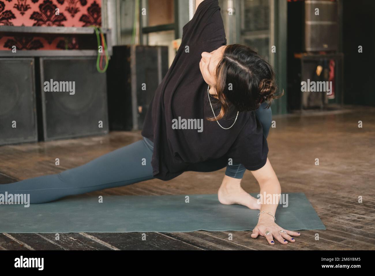 Femme yogi nouveau professeur jeune adulte faisant une pose de skandasana torsadée avec un bras au plafond portant des leggings verts dans sa pratique de yoga Banque D'Images