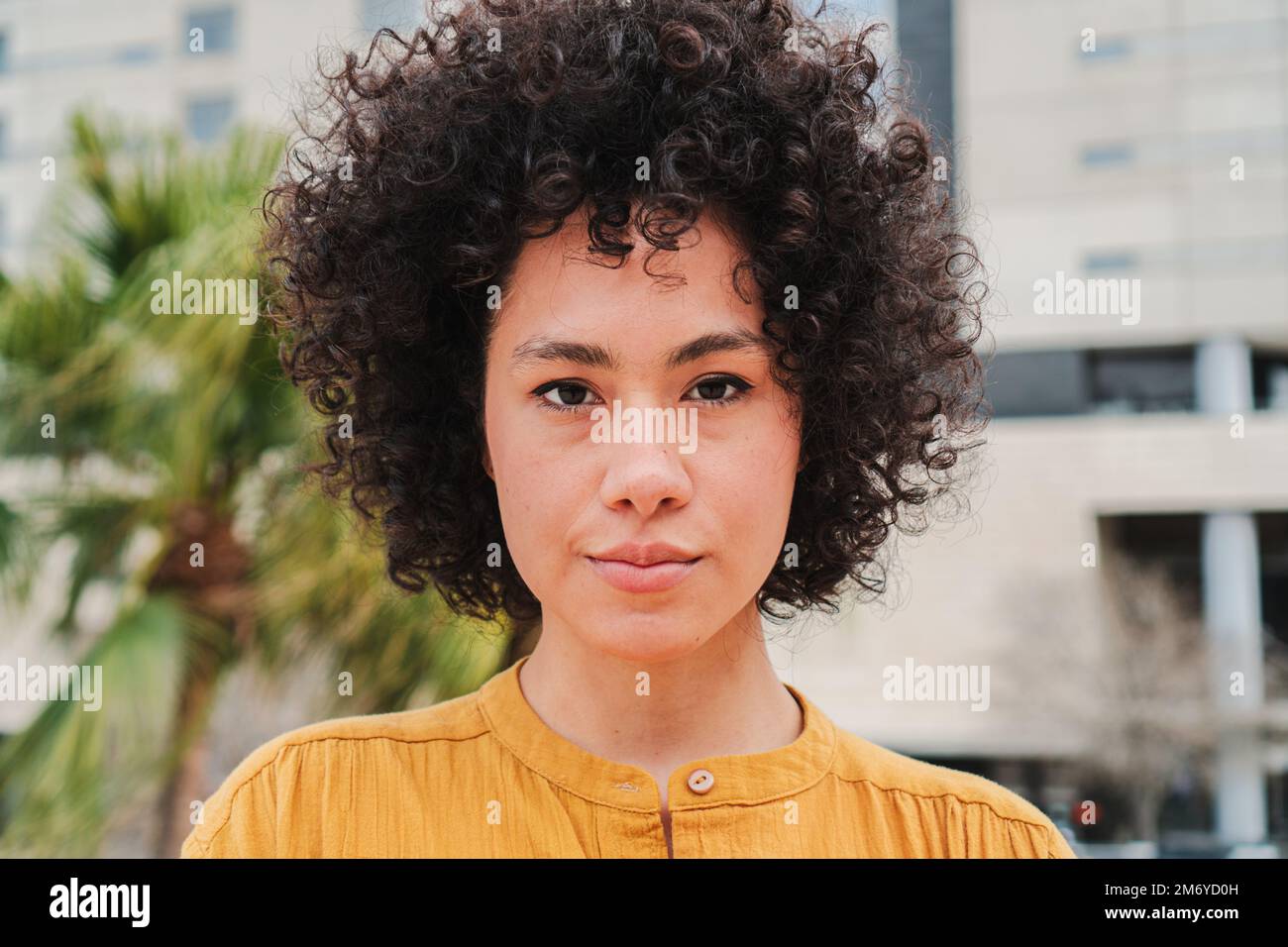 Gros plan d'une jeune femme hispanique avec des cheveux ondulés et bouclés regardant sérieusement l'appareil photo. Vue de face de la jolie dame latine brunette debout à l'extérieur. Photo de haute qualité Banque D'Images