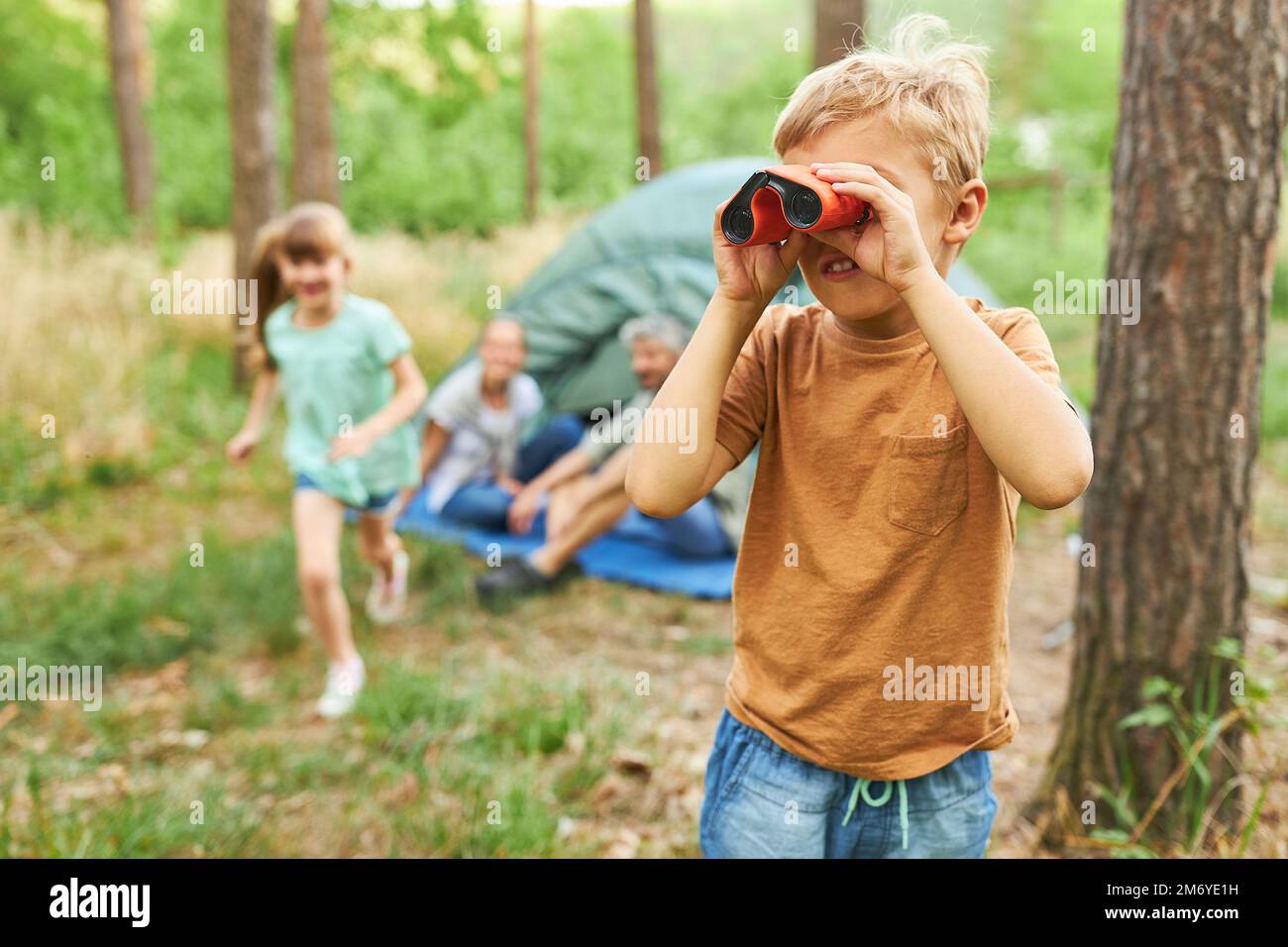 Garçon explorant à travers des jumelles avec la famille en arrière-plan au camping pendant les vacances Banque D'Images