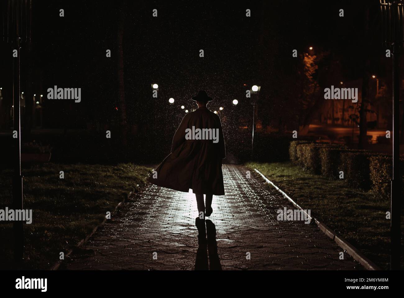 détective masculin dans un chapeau et imperméable la nuit dans une ville pluvieuse dans le style de film noir Banque D'Images