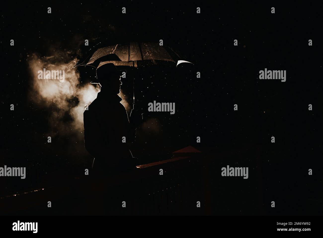 silhouette dans le style noir d'un détective mafieux masculin dans un imperméable et chapeau sous un parapluie une nuit de pluie Banque D'Images