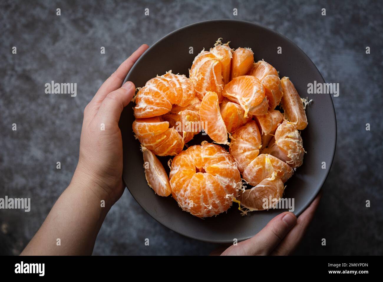 Mandarines dans un bol. Les mains d'une femme européenne tiennent une assiette de mandarines pelées. Mise au point sélective, photo sombre et sombre, faible profondeur de champ Banque D'Images