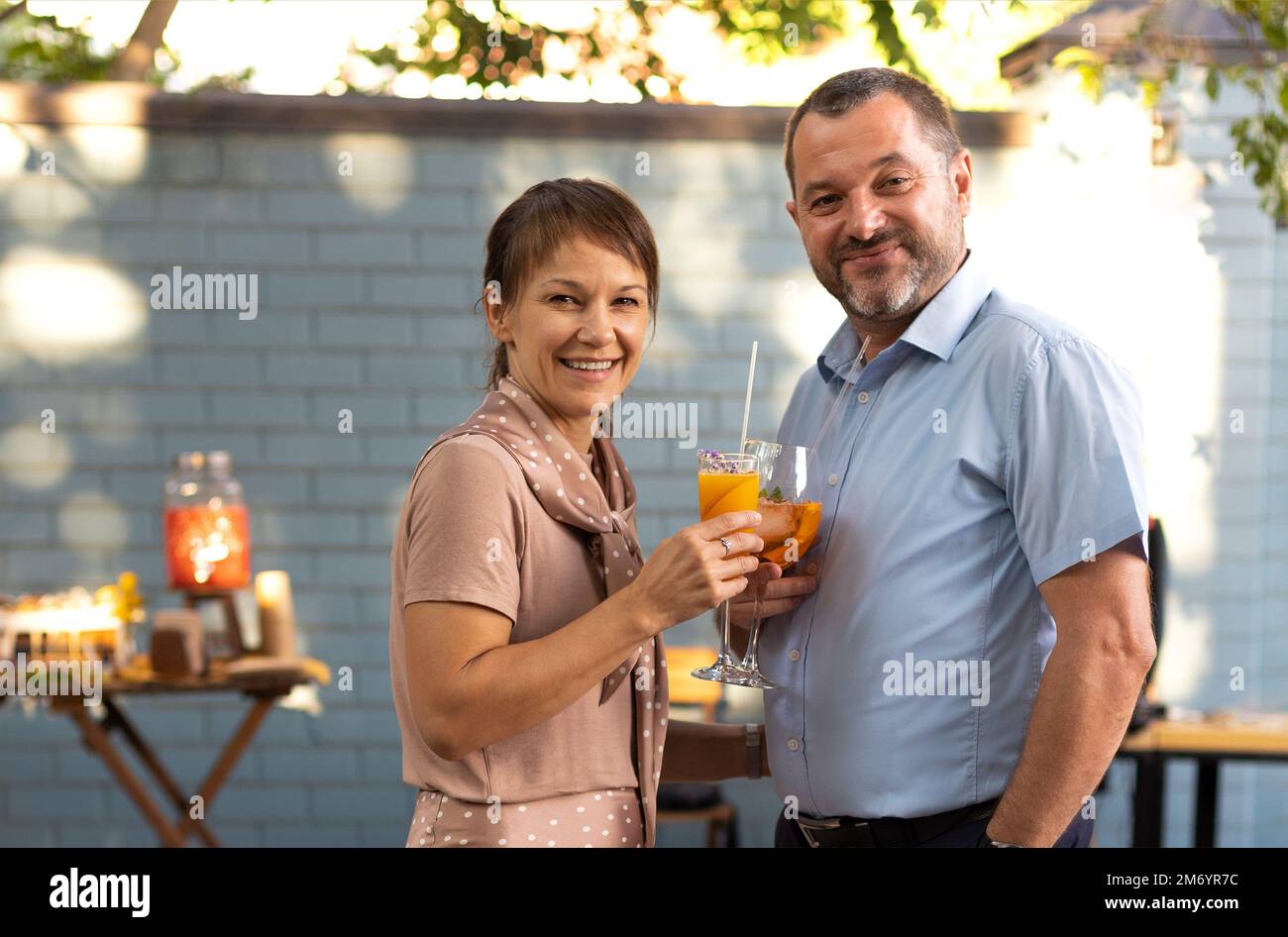 Couple heureux parlant et flirtant dans le jardin de la terrasse qui contient des cocktails. Les gens qui toaster le cocktail bellini et Aperol spritz ensemble à l'extérieur s Banque D'Images