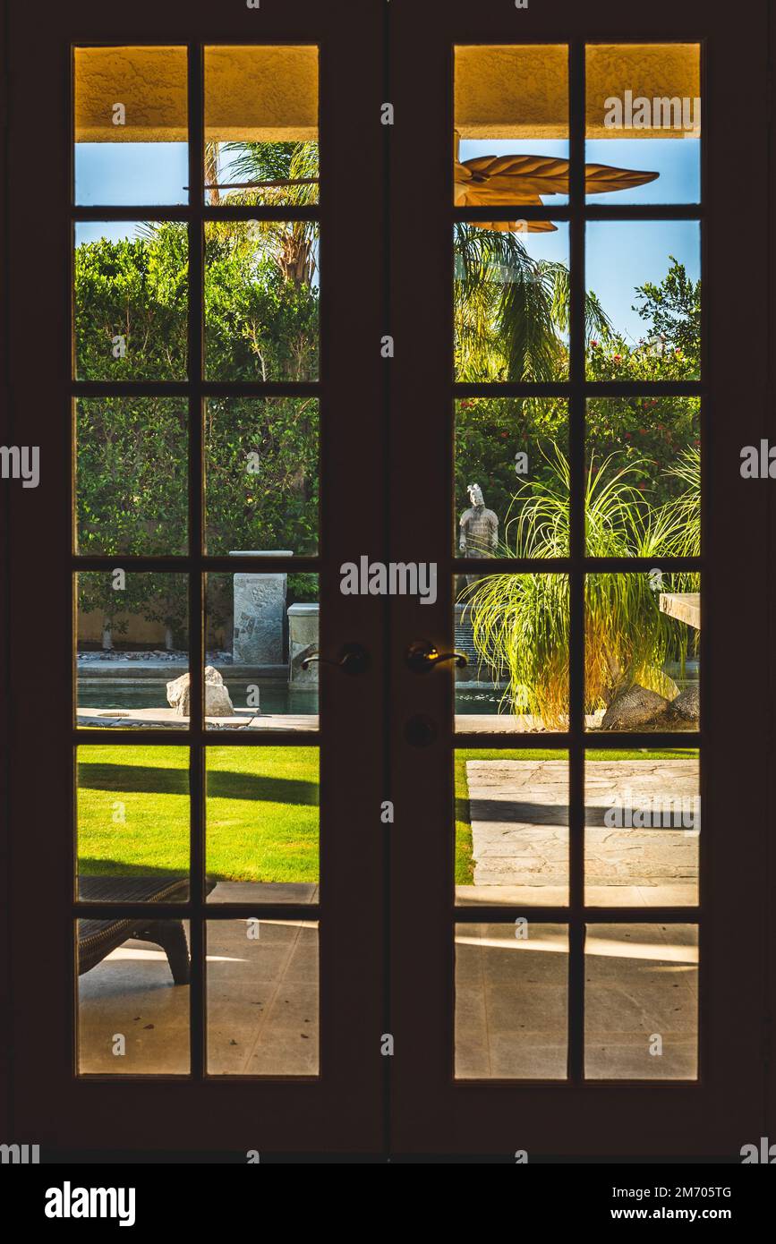 Une fenêtre à la française donnant sur le jardin avec une piscine et une pelouse bien entretenue par une journée ensoleillée, verticale Banque D'Images