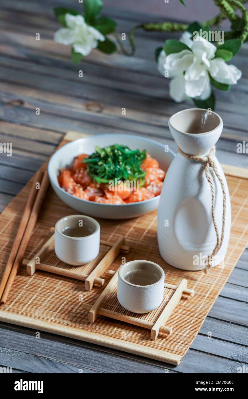 Saké japonais et saumon sashimi et algues wakame sur un tapis de bambou Banque D'Images