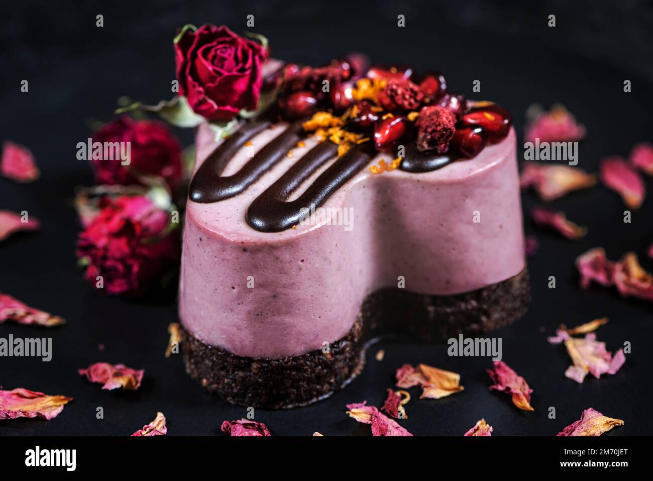 Gâteau au coeur décoré de grenade et de fraises. Dessert sur une assiette noire avec roses. Banque D'Images