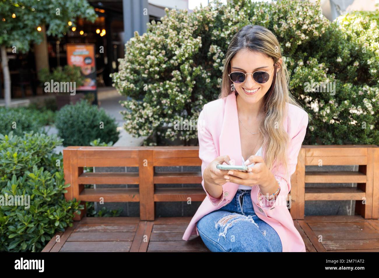 Jeune femme souriante, utilisant un smartphone à l'extérieur du centre commercial. Internet et la dépendance aux médias sociaux Banque D'Images