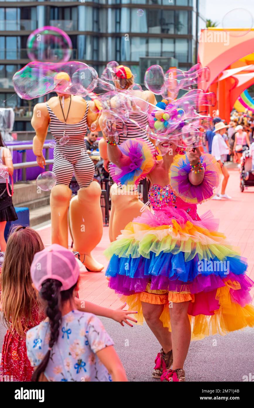 Un artiste dans une robe aux couleurs vives crée beaucoup de bulles flottantes dans l'air pour regarder les jeunes enfants Banque D'Images