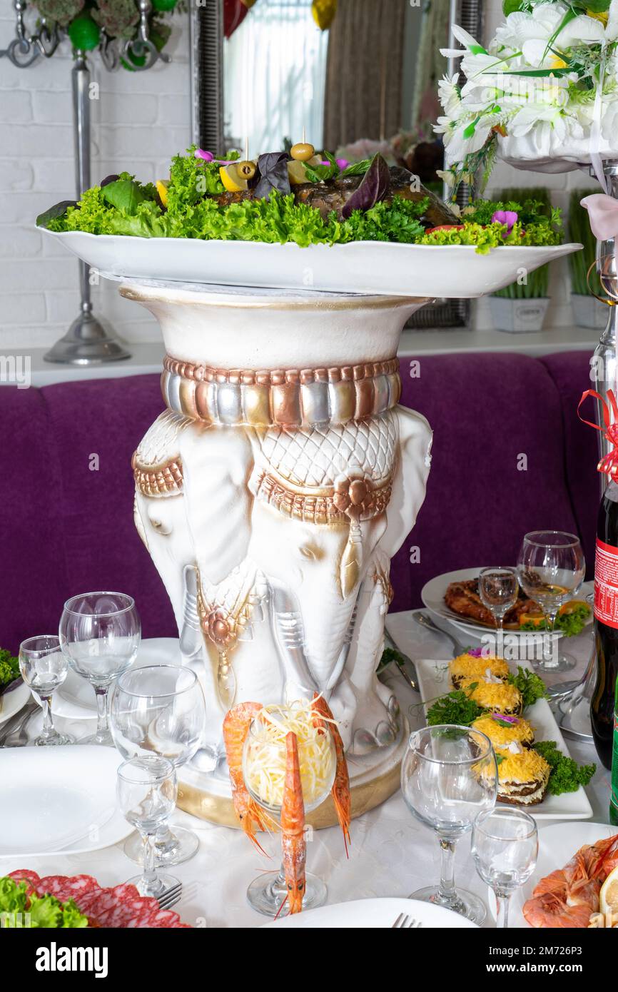Poisson farci décoré de légumes verts et de citrons sur la table de fête. Un grand vase blanc sur la table de fête. Banque D'Images
