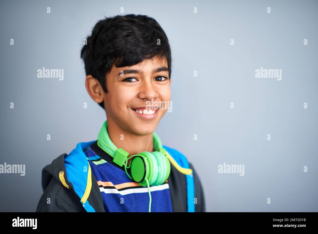 Je garde toujours ma musique proche. Un adorable jeune préadolescent debout et souriant sur fond gris. Banque D'Images